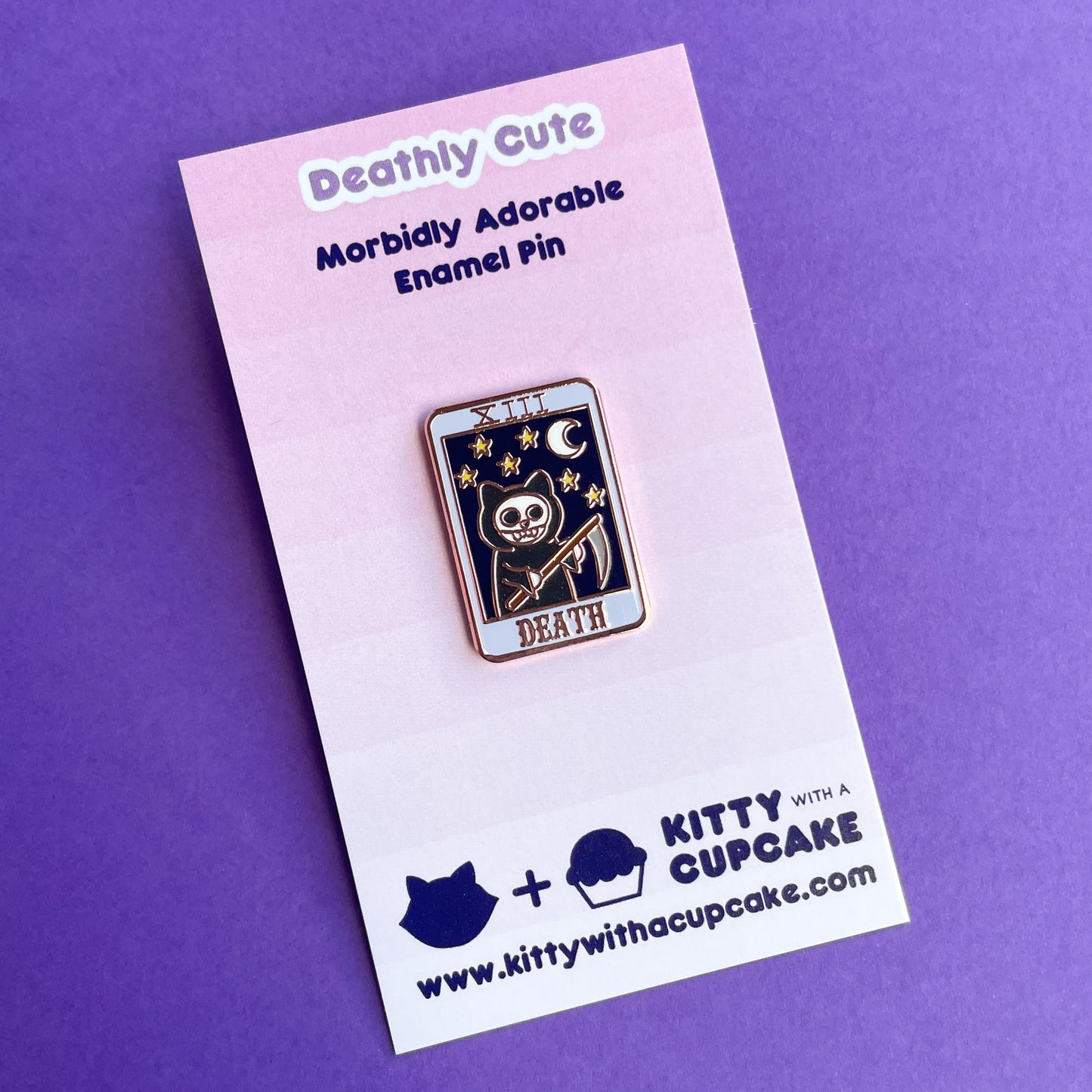 An enamel pin shaped like a tarot card with a grim reaper cat with a night sky on it and the word "Death" on a pink card.