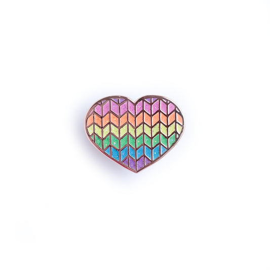 A heart shaped enamel pin with a glittery rainbow knit pattern.
