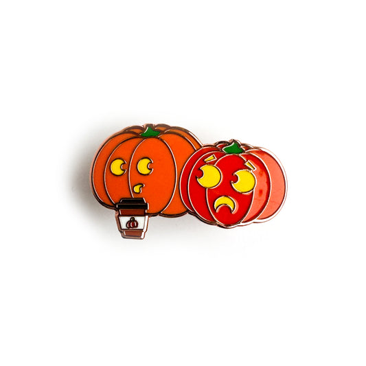 An enamel pin shaped like two pumpkins, one is drinking a pumpkin spice latte.
