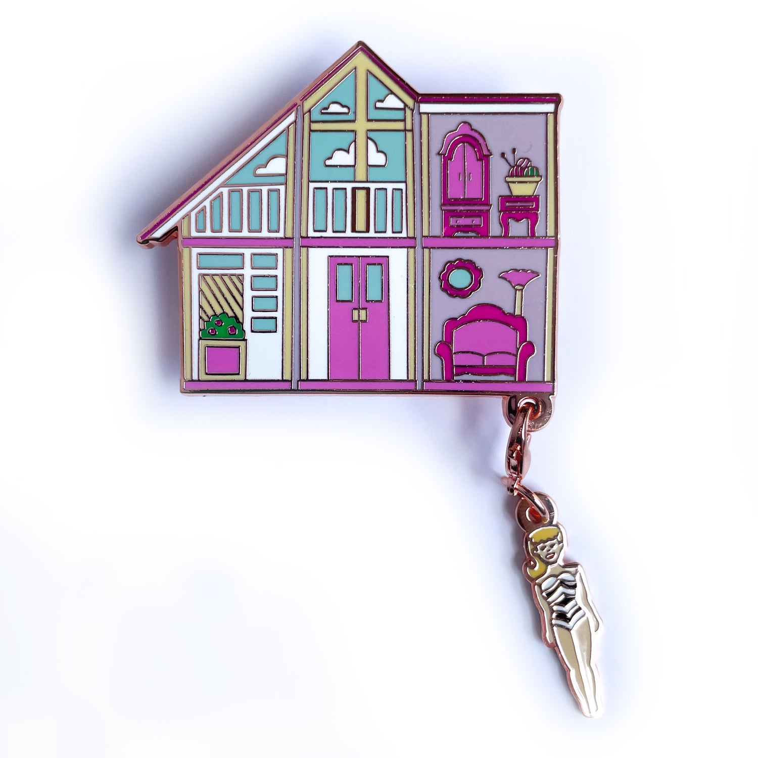 An enamel pin of a pink doll house with a Barbie shaped charm hanging from the corner.