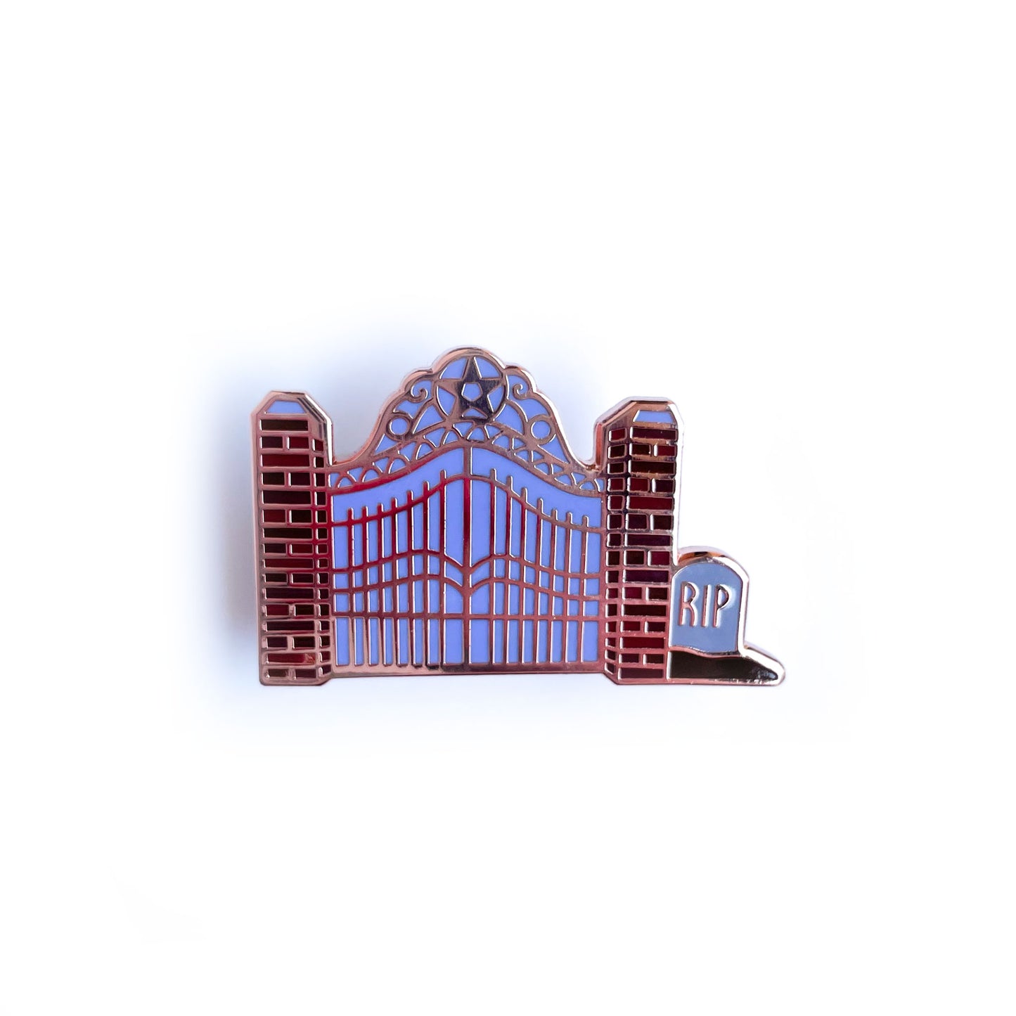 An enamel pin shaped like a cemetery gate with brick pillars and a tombstone that reads "RIP" 