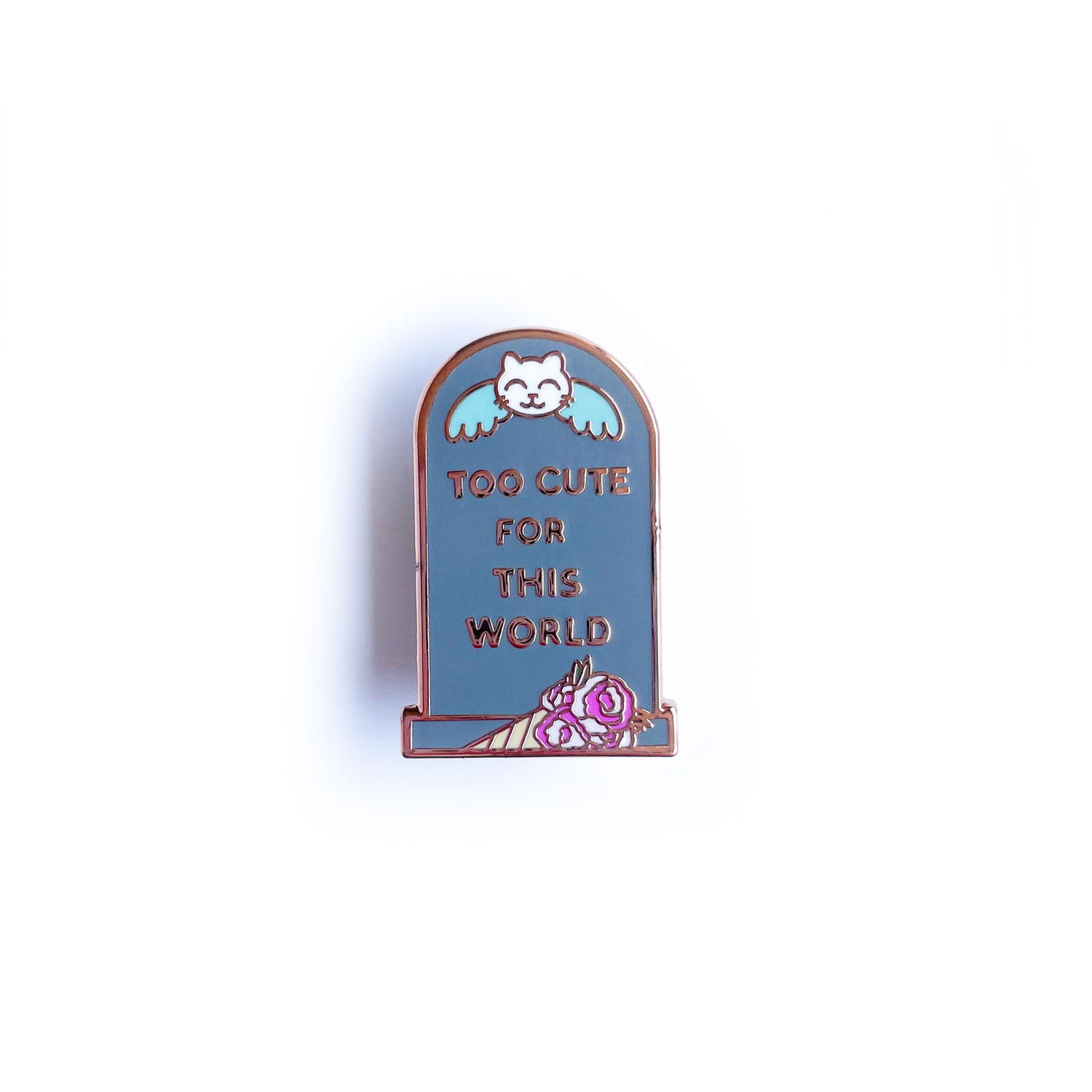A headstone shaped enamel pin that reads "Too Cute For This World" with a cat angle on it and a bouquet by it.