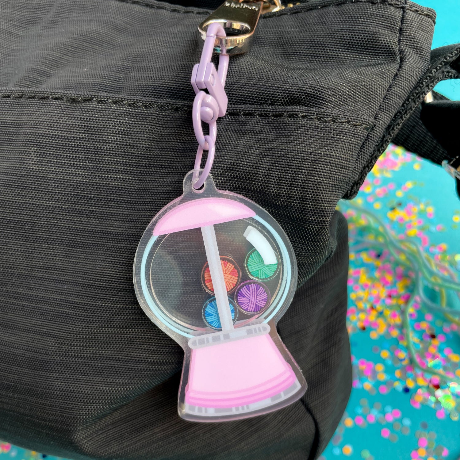A gumball machine keychain attached to a black purse. 
