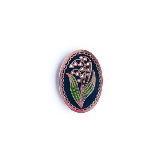 An enamel pin shaped like an oval with a lily of the valley in it.