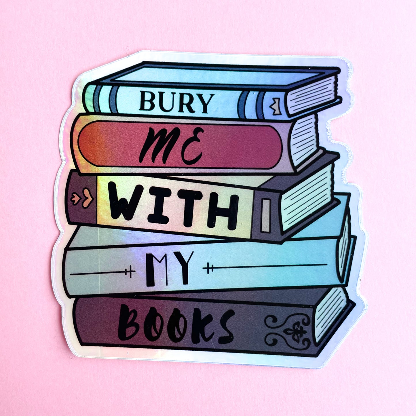 A sticker shaped like a stack of books that reads "Bury me with my books" on a pink background.