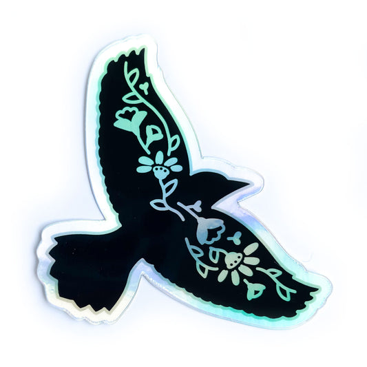 A holographic sticker shaped like the silhouette of a raven with flowers along its wingspan