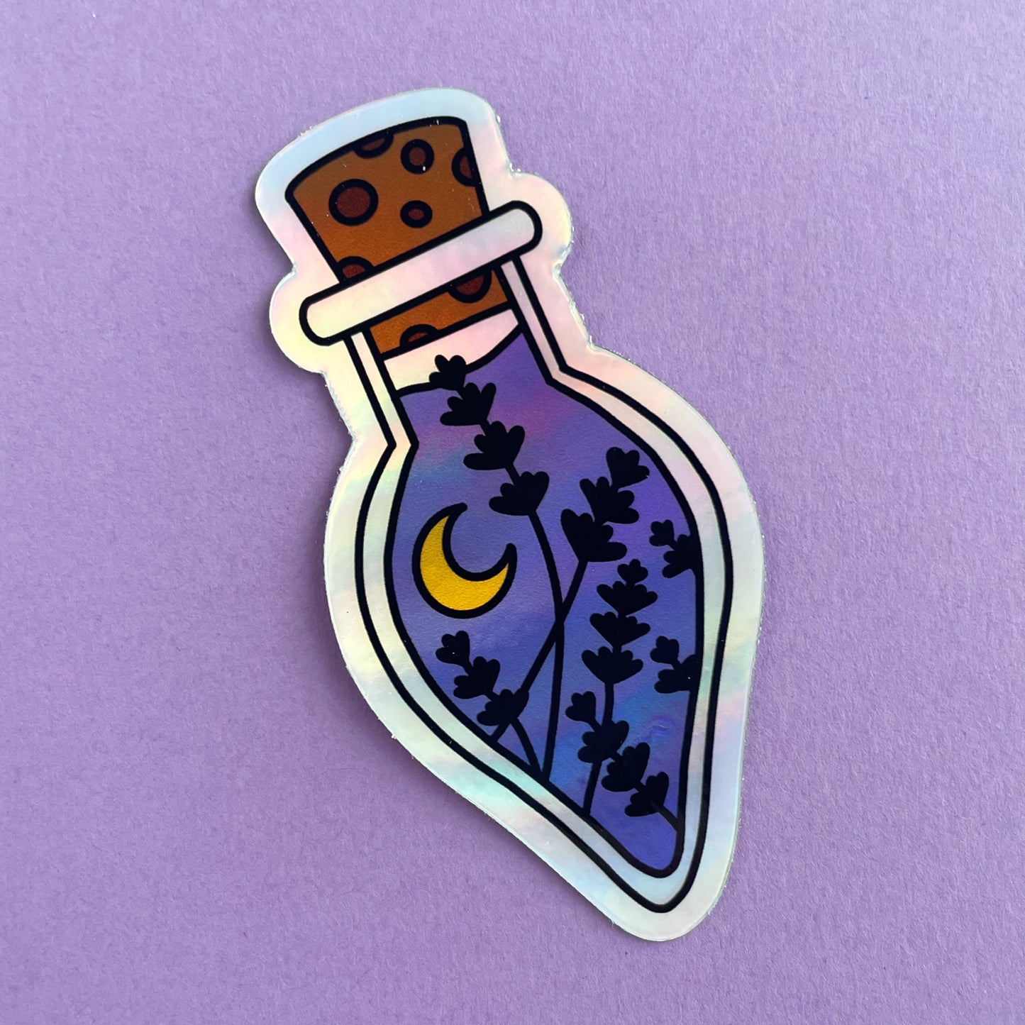 A holographic sticker in the shape of a tear drop shaped potion bottle. The bottle has a cork and is filled with purple liquid, flowers, and a crescent moon. The sticker is on a lavender background.