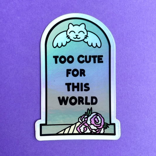 A headstone shaped holographic sticker that reads "Too Cute For This World" with a cat angle on it and a bouquet by it. The sticker is displayed on a dark purple background