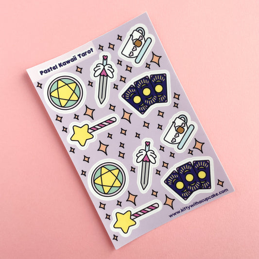A sticker sheet with a lavender background with stickers that are cute versions of the four tarot suits, pentacles, swords, cups, wands, plus 3 fanned cards. The sticker sheet is on a pink background.