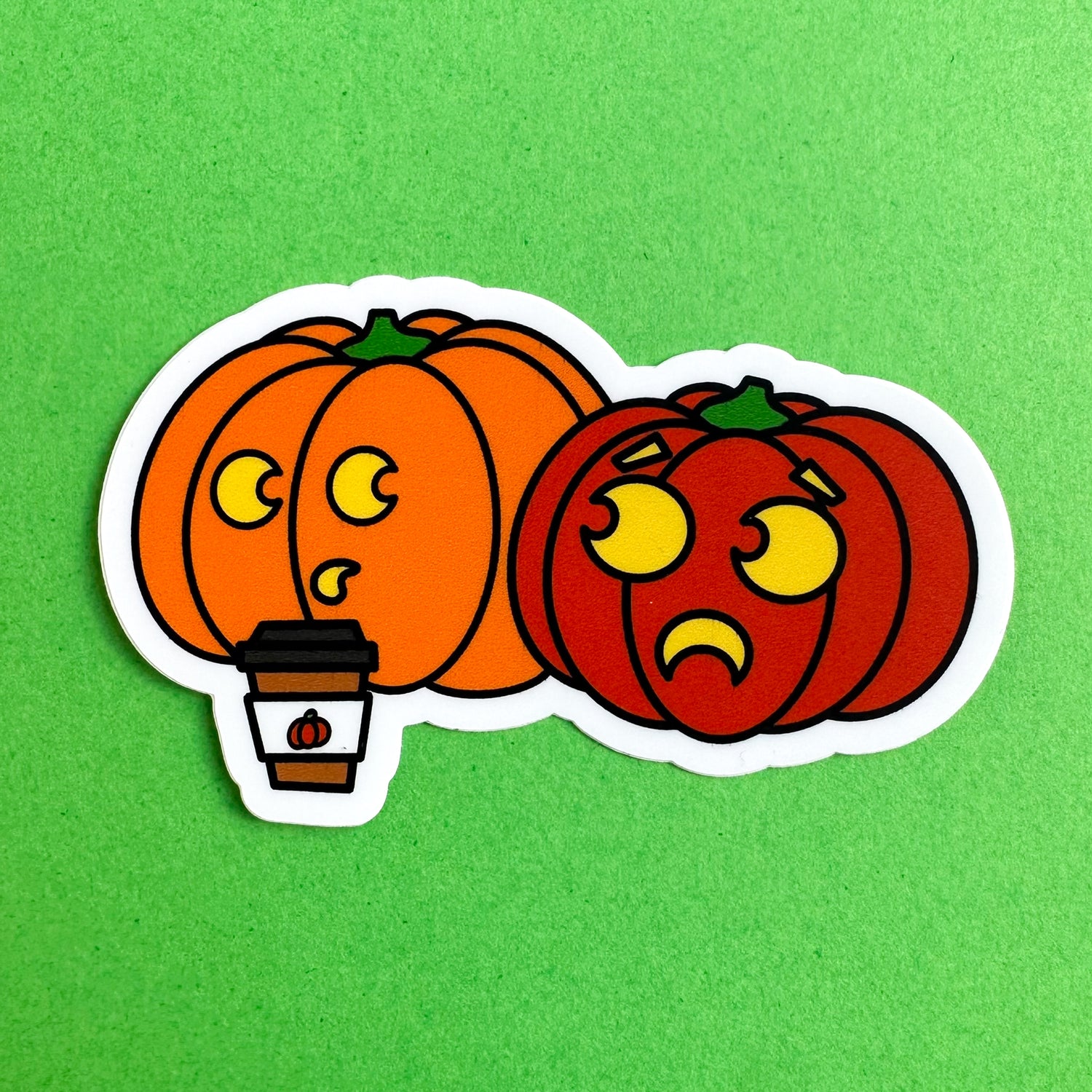 A sticker shaped like two pumpkins with one drinking a pumpkin spice latte on top of a green background.