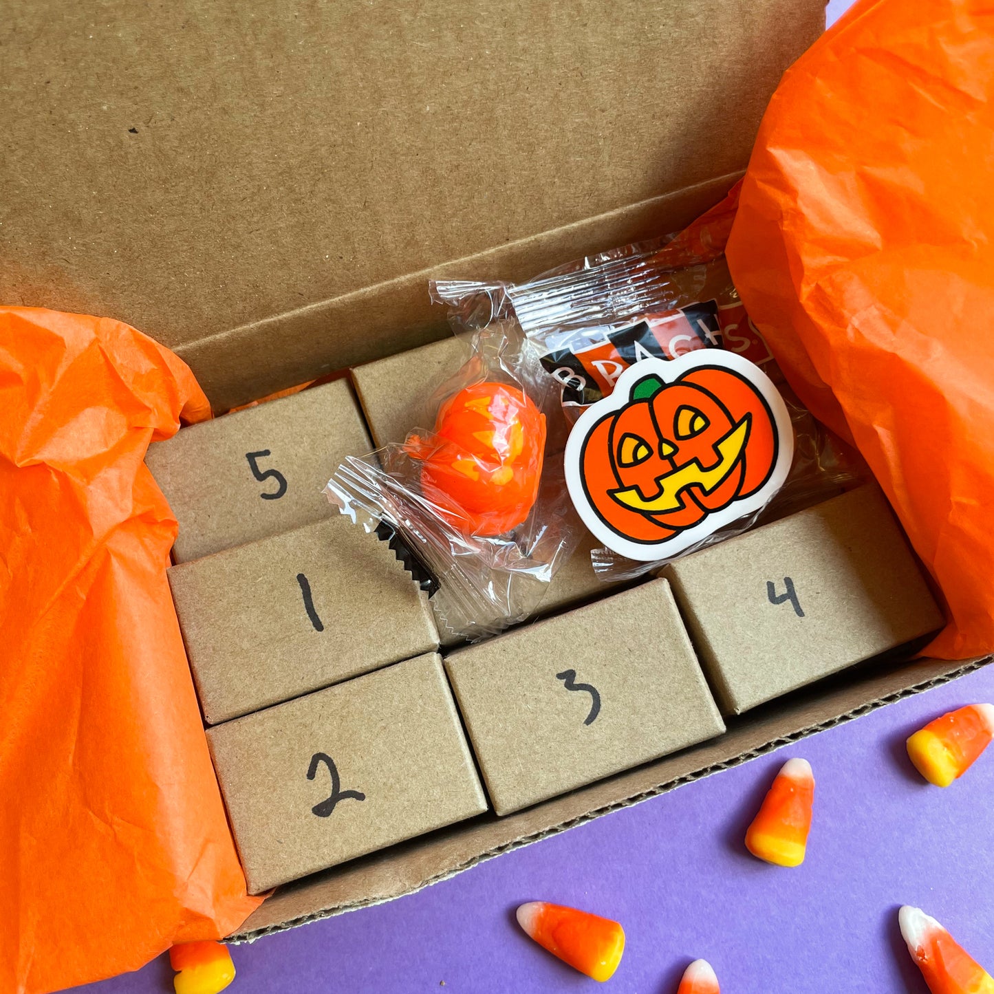 A box with small numbered Kraft paper boxes inside with a jack o lantern sticker and candy corn around it. 