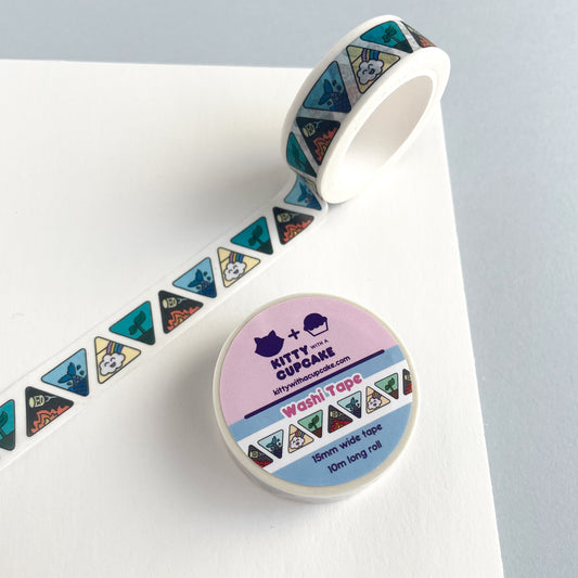 A roll of Elemental Washi Tape over a white piece of paper.  The tape has a white background with alternating upside down and right side up triangles. The triangles feature cute symbols for each of the four elements. A happy cloud and rainbow for air, a sprouting plant for earth, a marshmallow over a flame for fire, and a mermaid tail splashing for water.