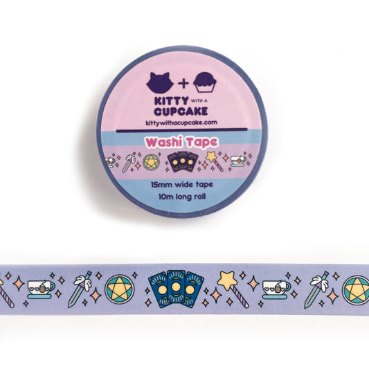A washi tape roll. The tape features small tarot cards, a star wand, a teacup, a sword, and a pentacle all in pastel colors. There are orange pastel sparkles in between the items on a lavender background.