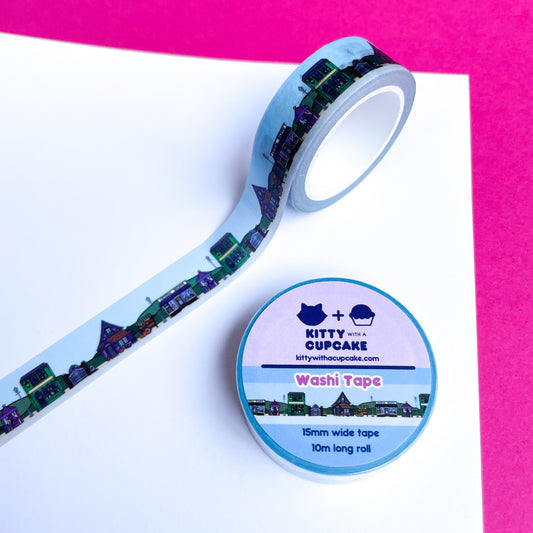 A blue washi tape with an illustration of a magically themed town street displayed on white and pink construction paper